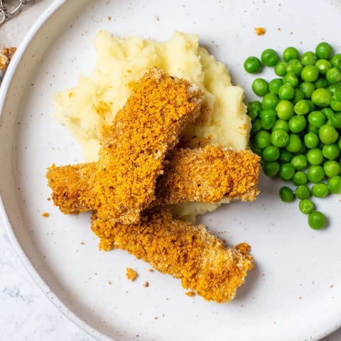Gebackene Fischstäbchen mit cremigem Kartoffelpüree und Erbsen – ein köstliches Familienessen.