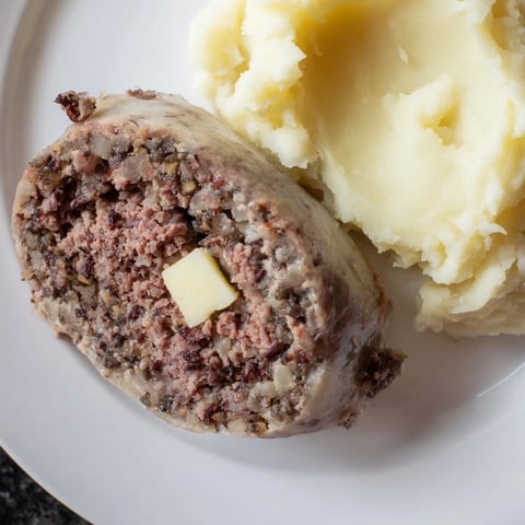 A slice of savory Scottish haggis, steaming and served with mashed neeps and tatties.