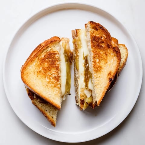 Goldbraun gebratenes Havarti & Caramelized Leek Grilled Cheese liegt halbiert auf einem rustikalen Holztisch, mit zarten Röstspuren und einer leichten Oberschicht.