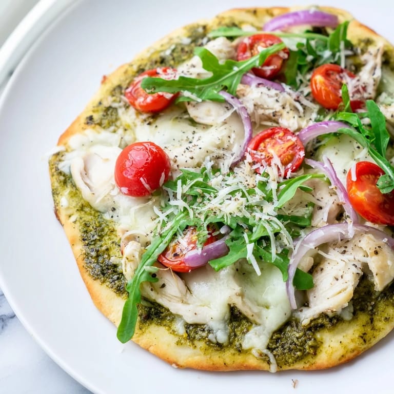 Golden-crusted Pesto Chicken Flatbread piled high with fresh arugula and basil for serving.