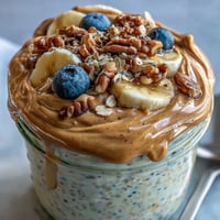 High-Protein Peanut Butter Overnight Oats im Glas mit frischen Erdbeeren und Bananenliebchen garniert